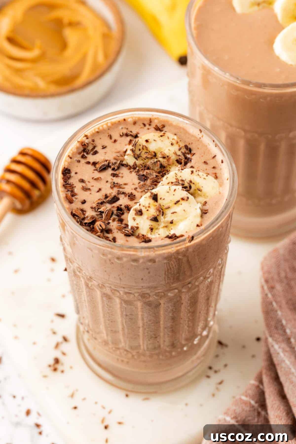Indulgent Chocolate Peanut Butter Banana Smoothie 2 chocolate peanut butter banana smoothie topped with chocolate shavings and banana slices, ready to be enjoyed