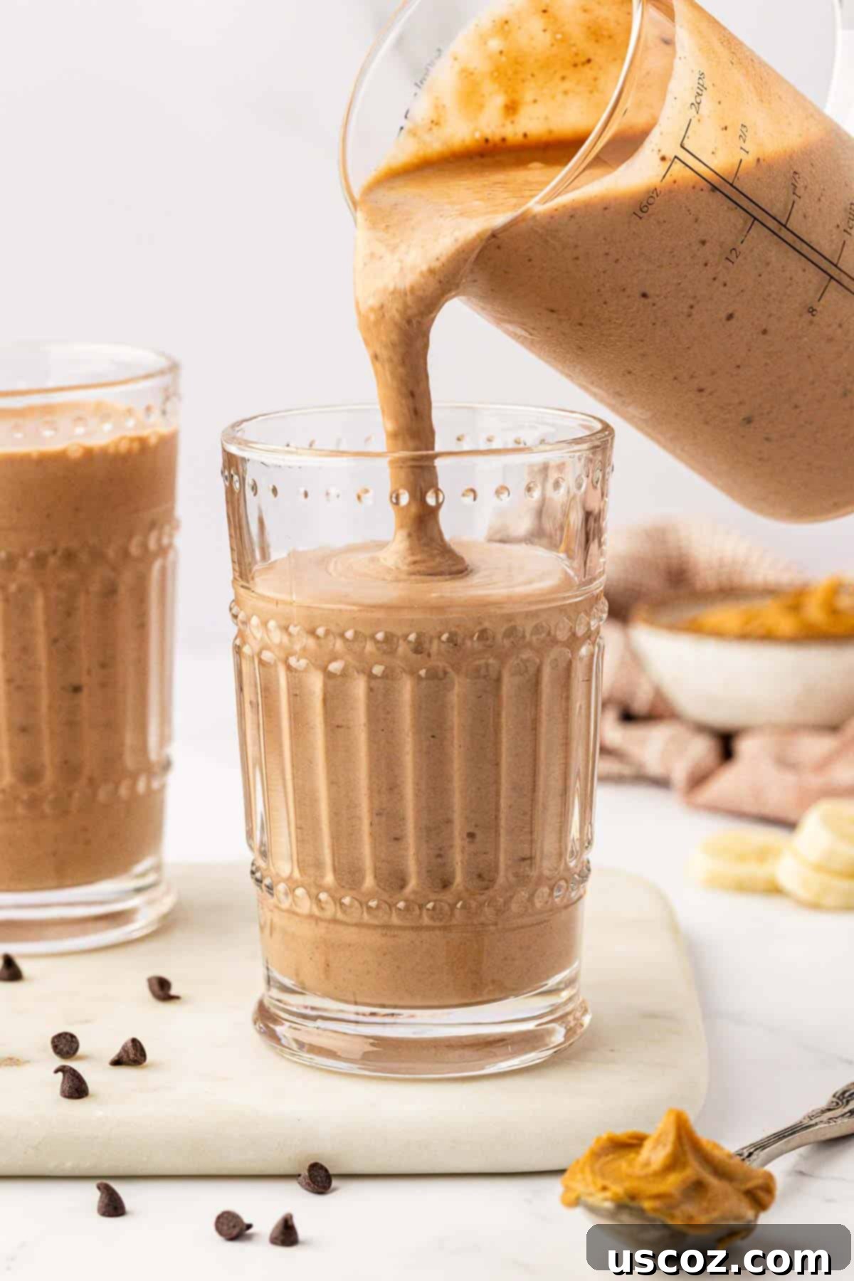 Indulgent Chocolate Peanut Butter Banana Smoothie 7 A chocolate peanut butter banana smoothie being poured from a blender into a glass, showing its thick, creamy texture