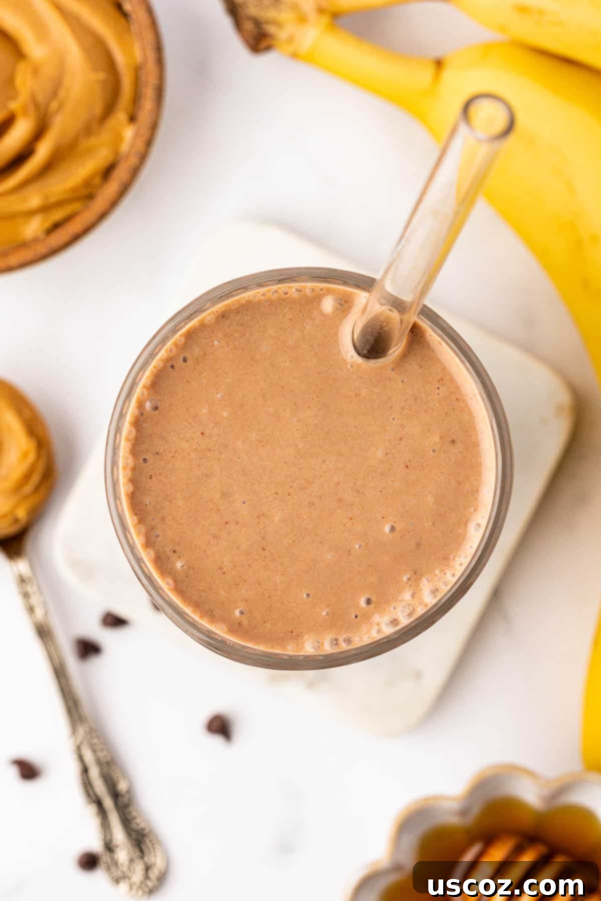 Indulgent Chocolate Peanut Butter Banana Smoothie 8 chocolate peanut butter banana smoothie in a clear glass with a straw, garnished with a banana slice and chocolate shavings