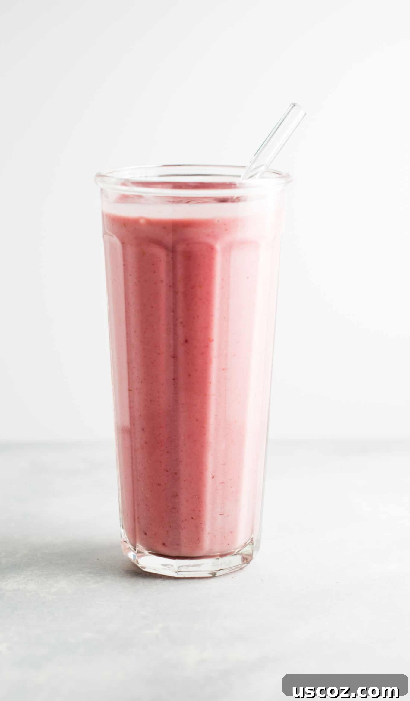 strawberry banana yogurt smoothie in a glass, with a single strawberry on the rim