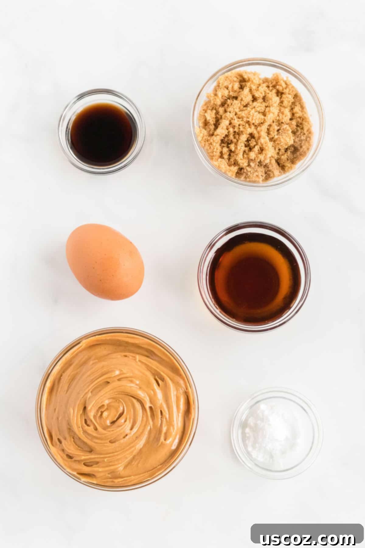 Irresistible Gluten-Free Peanut Butter Cookies 3 All six key ingredients laid out on a white surface: natural creamy peanut butter, an egg, light brown sugar, baking soda, vanilla extract, and pure maple syrup, ready for making gluten free peanut butter cookies.