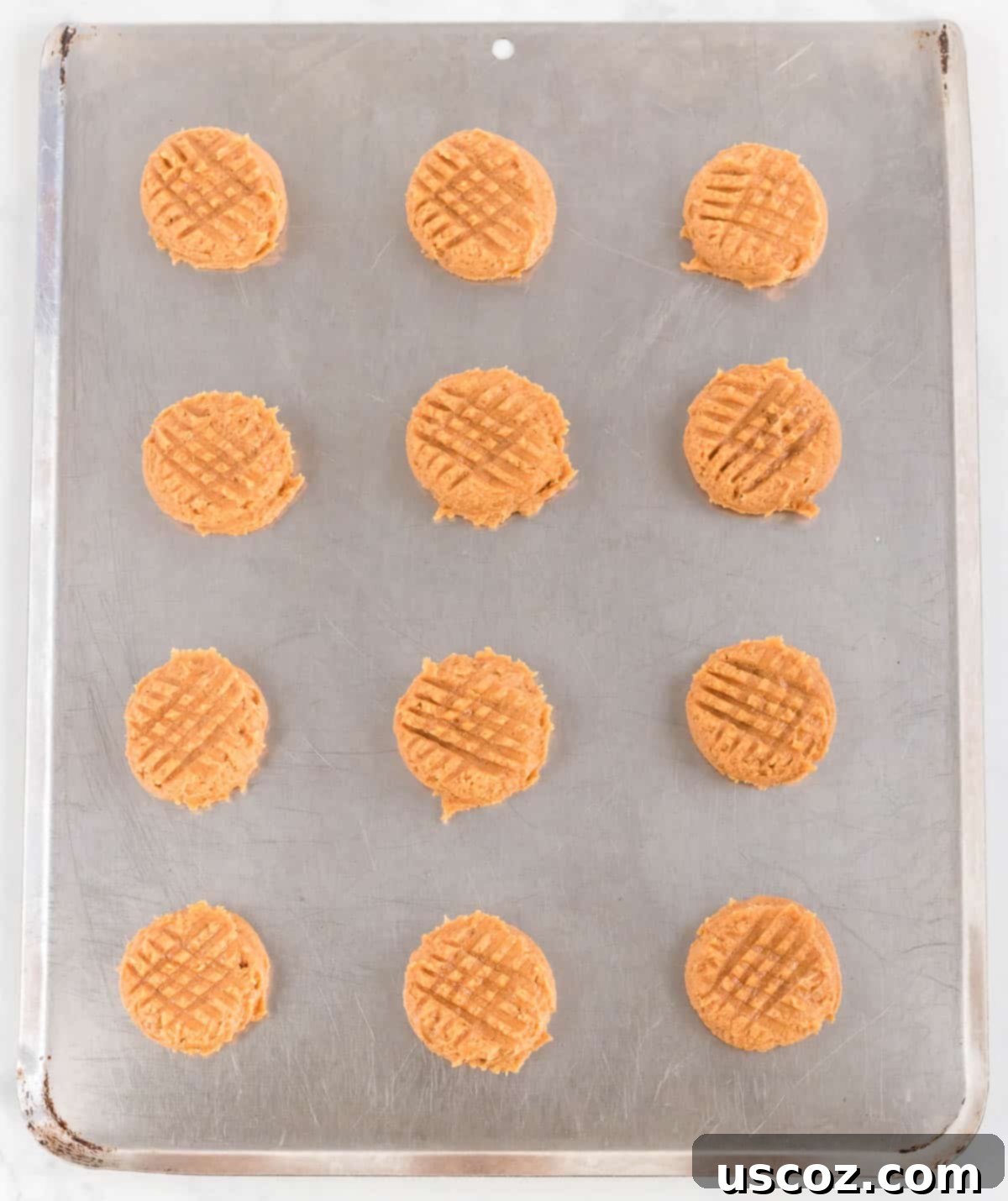 Irresistible Gluten-Free Peanut Butter Cookies 7 Close-up of gluten free peanut butter cookie dough balls on a baking sheet, each pressed with a fork to create the distinctive criss-cross pattern before baking.