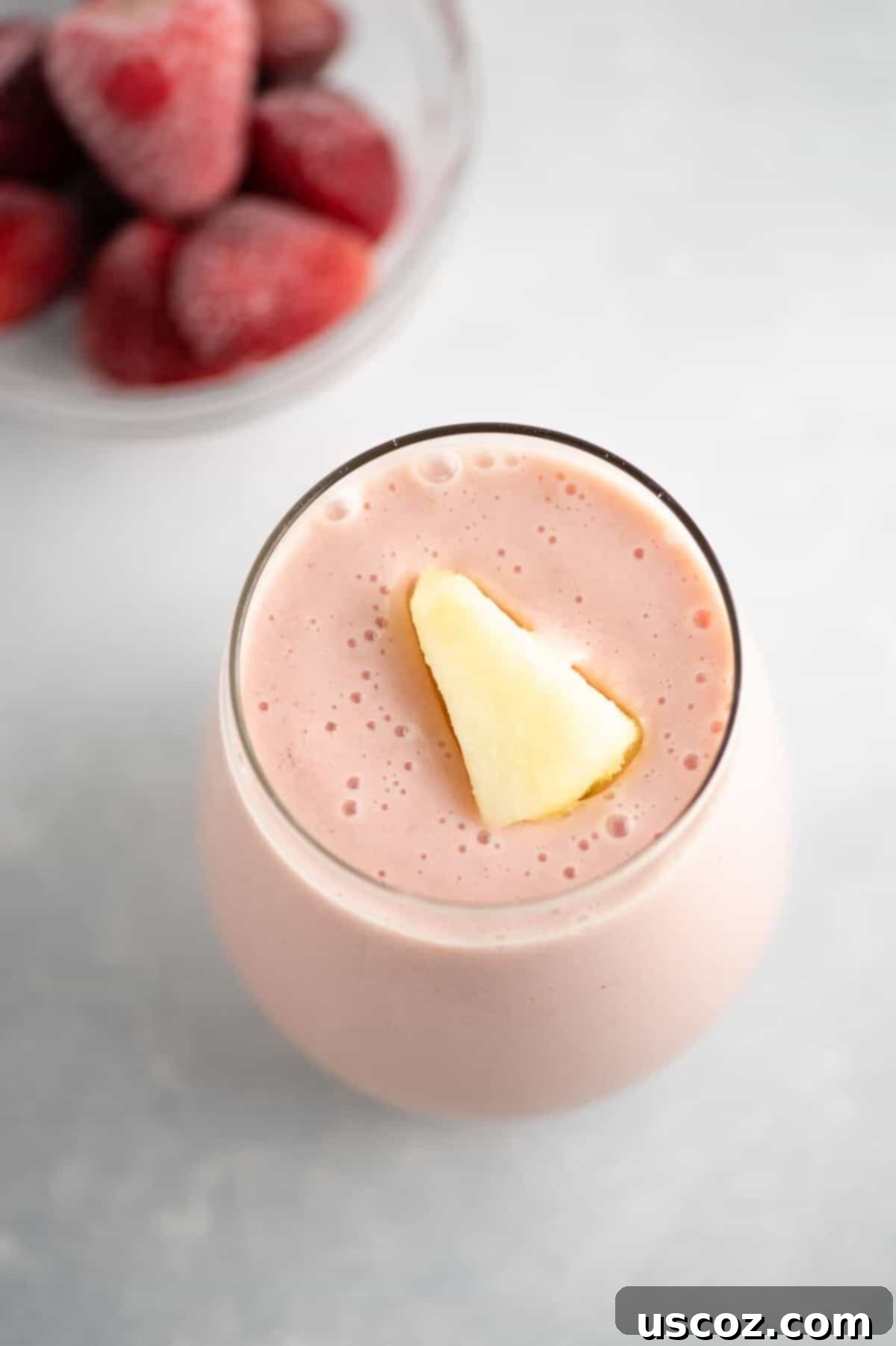A vibrant strawberry pineapple smoothie in a tall glass, garnished with a piece of frozen pineapple, highlighting its creamy texture and freshness.