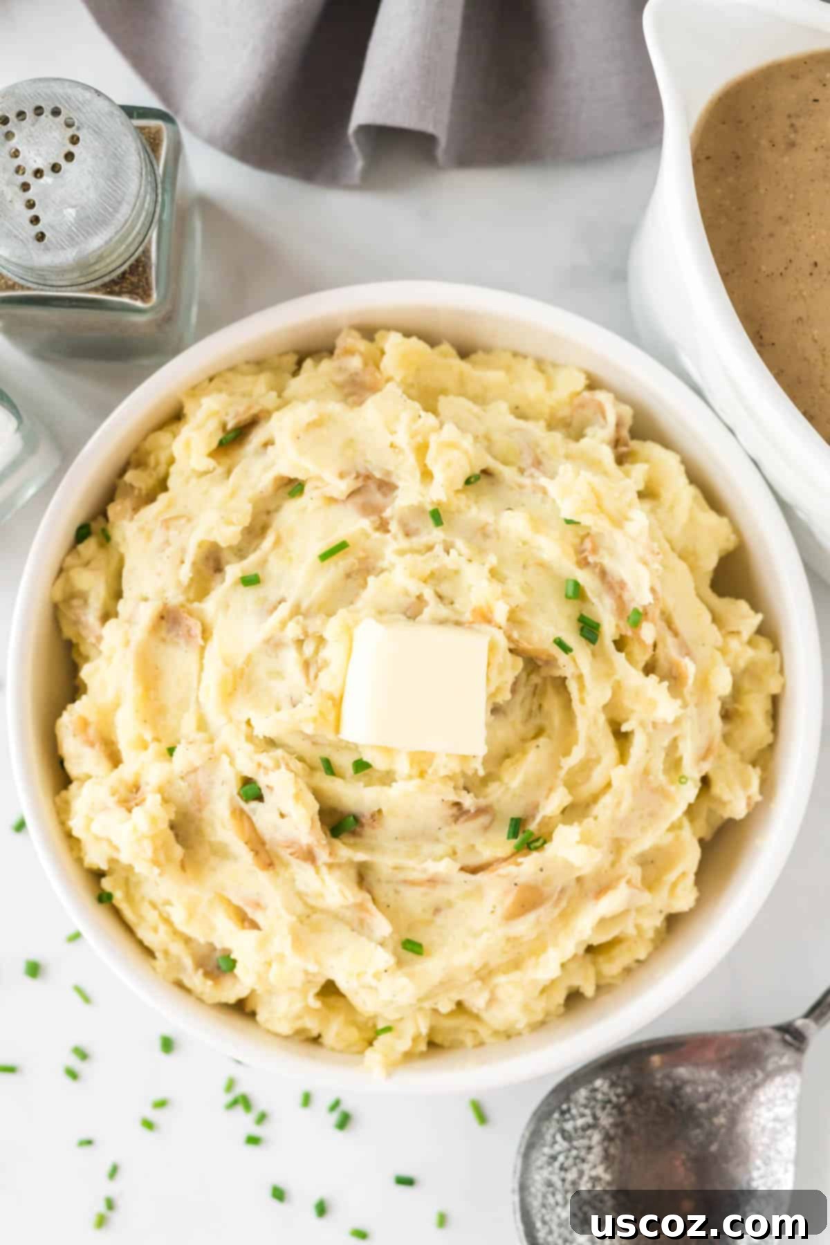 Tangy Mashed Potatoes 2 mashed potatoes in a bowl topped with butter and chives