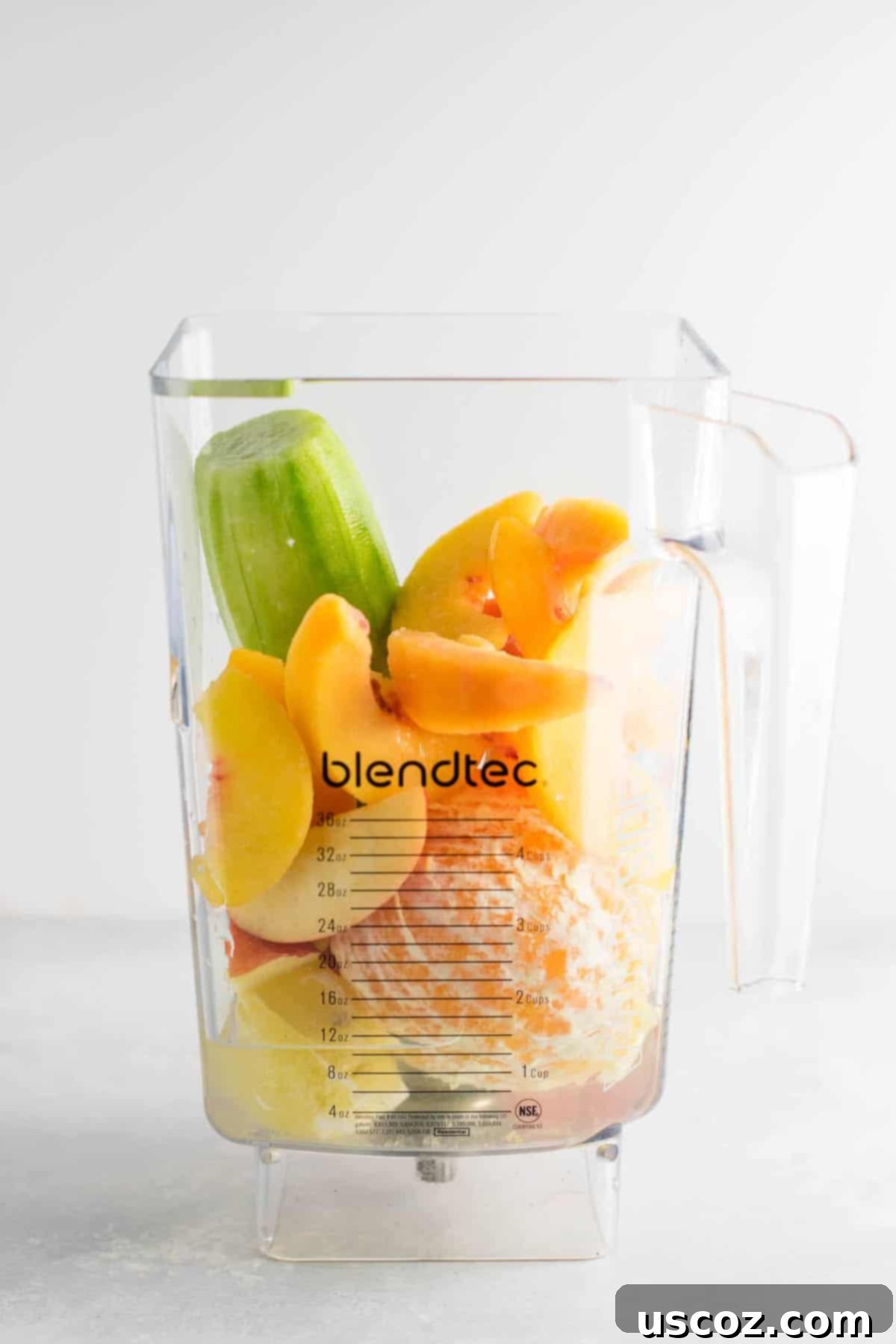 Fresh ingredients including cucumber, lemon, apples, orange, peaches, and water being added to a blender for a detox smoothie.