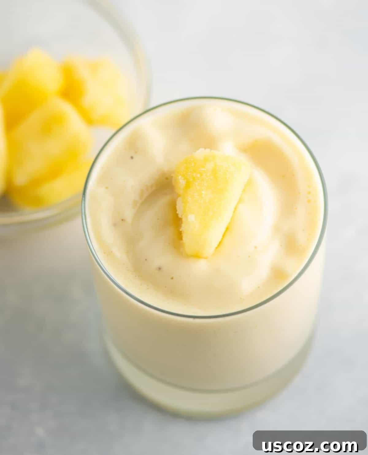 Refreshing pineapple smoothie in a glass, garnished with a piece of frozen pineapple.