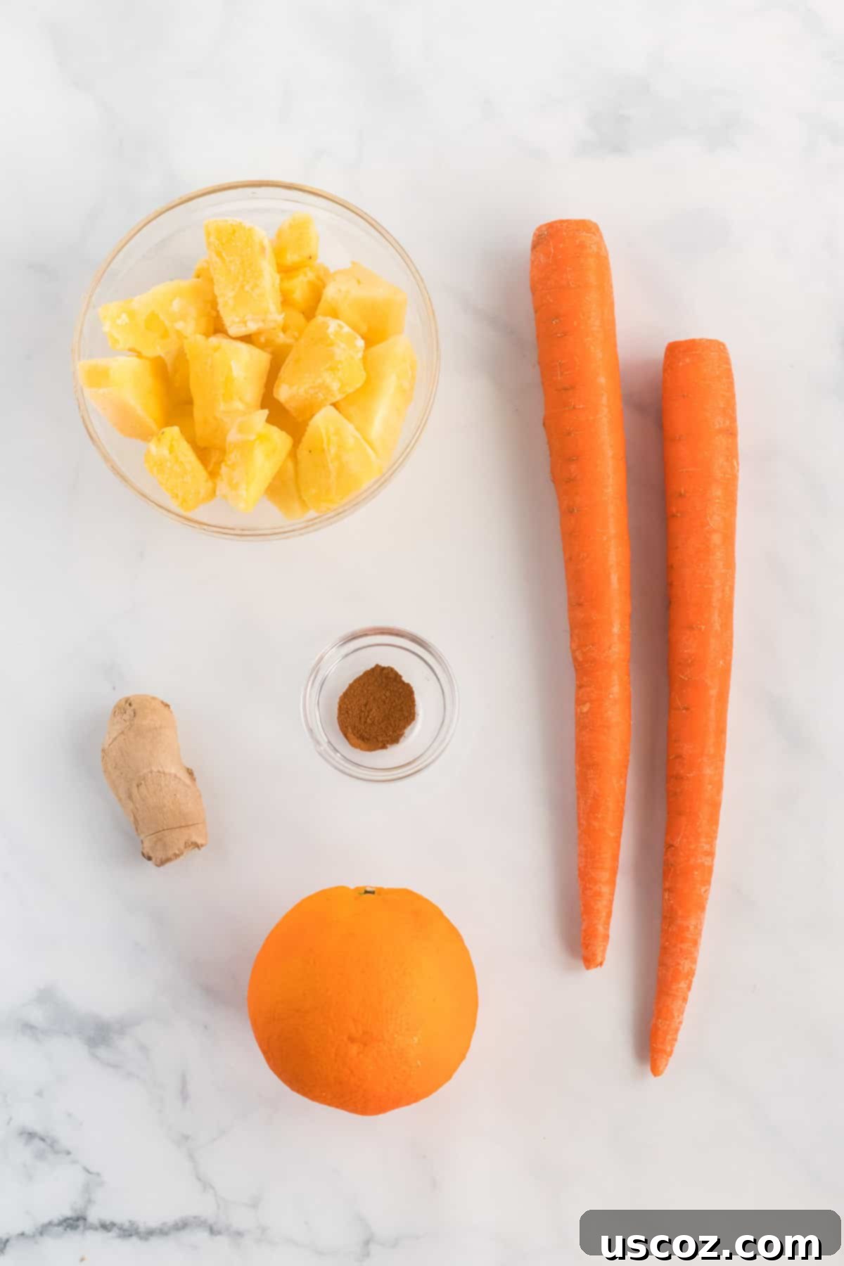 Golden Carrot Orange Smoothie 4 A vibrant selection of fresh ingredients laid out: bright carrots, a juicy orange, golden frozen pineapple chunks, a knob of fresh ginger, and a sprinkle of cinnamon, ready to be blended into a healthy smoothie.