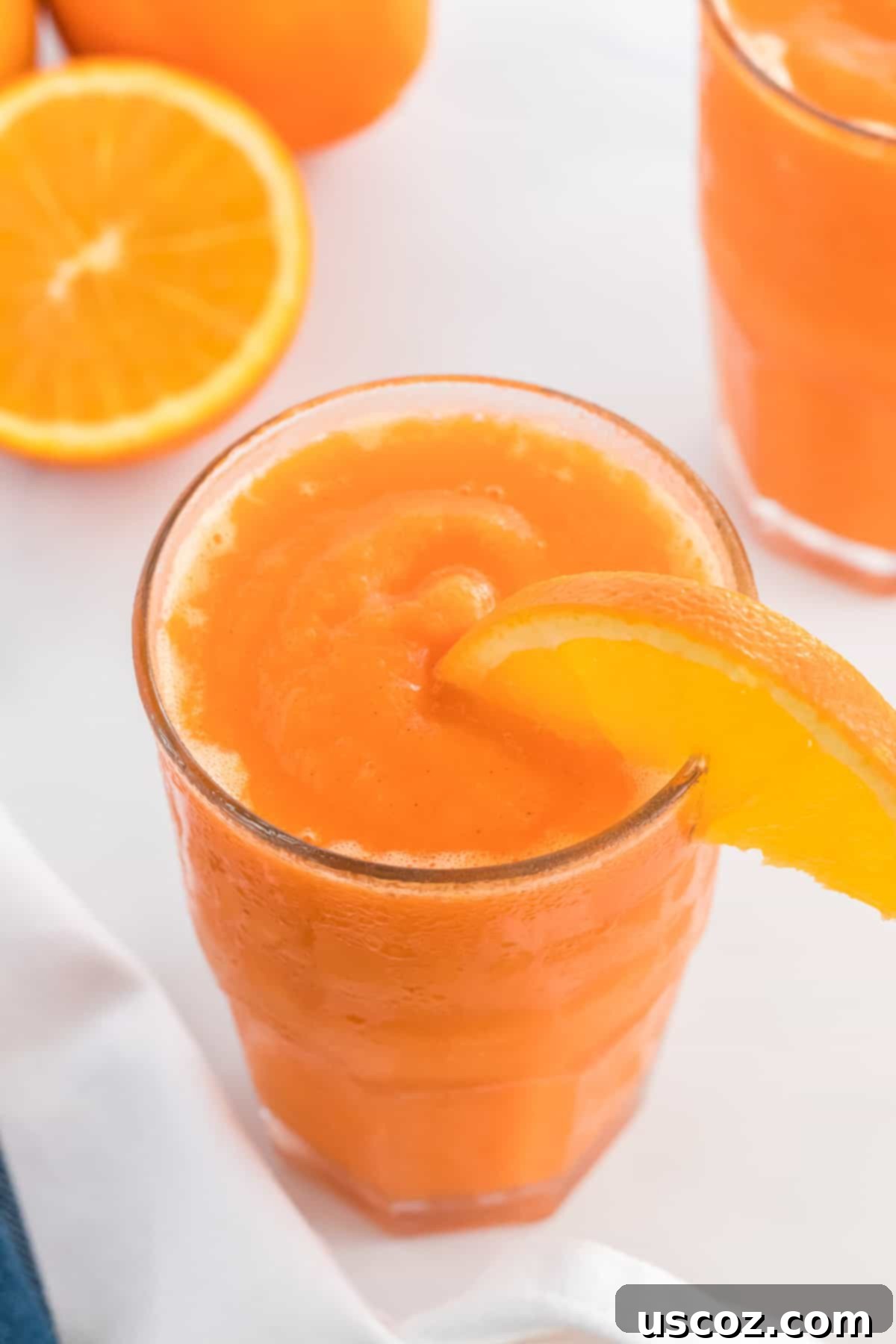 Golden Carrot Orange Smoothie 8 Two glasses of bright orange carrot orange smoothie, one with an orange slice garnish, presented on a light background, highlighting its vibrant color and freshness.