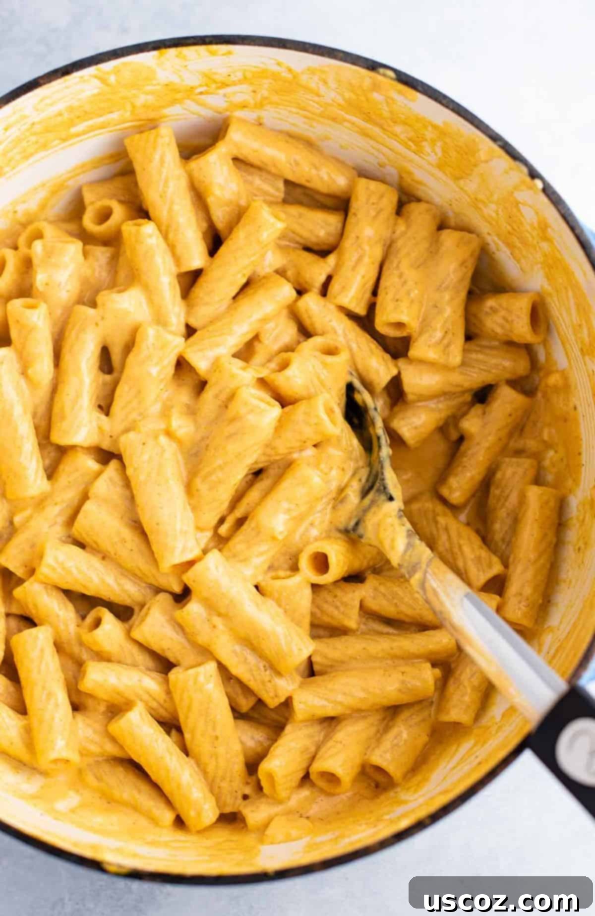 Rigatoni pasta coated in creamy pumpkin sauce, ready to be served from a large dish with a spoon.