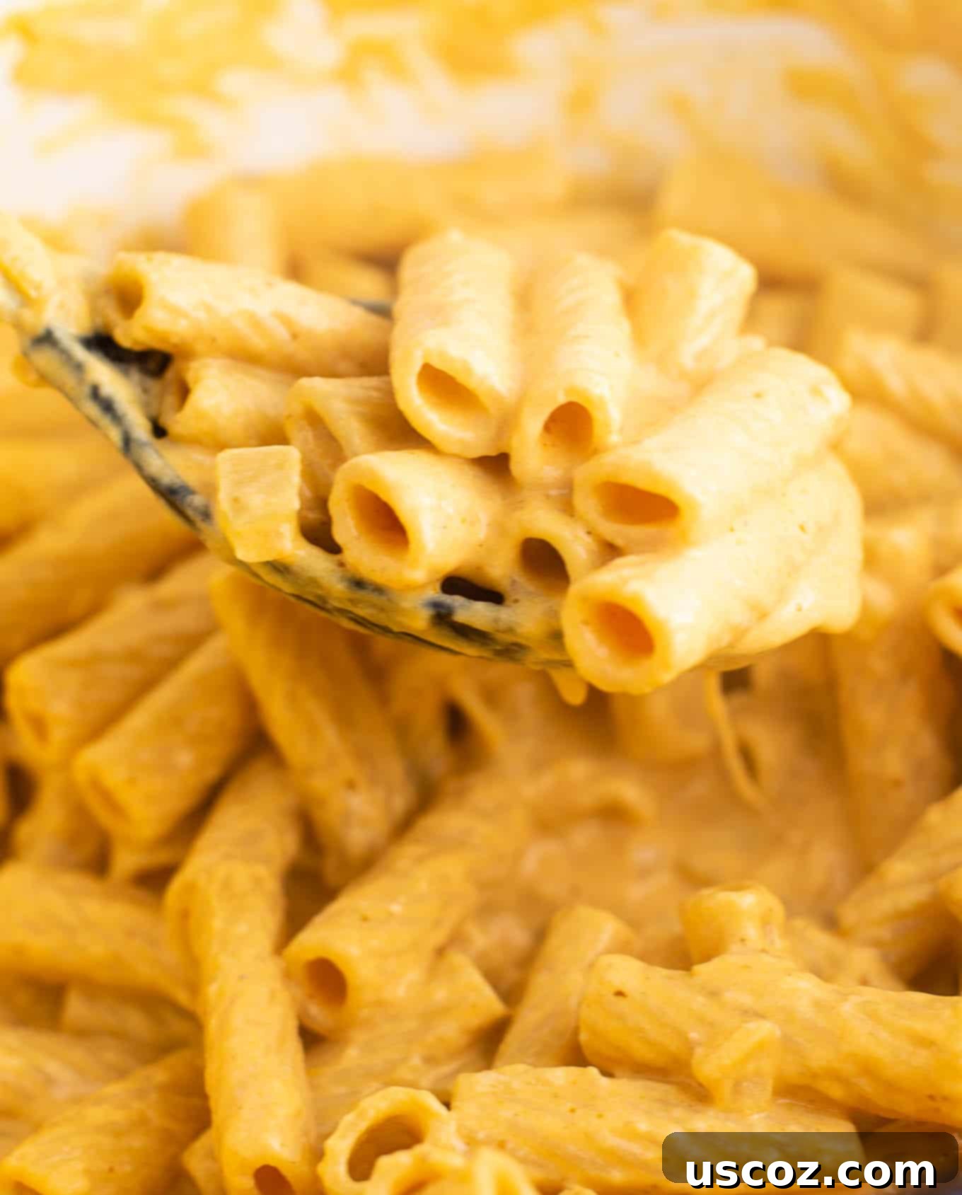 A spoonful of creamy pumpkin pasta held over the pot, showing the rich sauce coating the rigatoni.