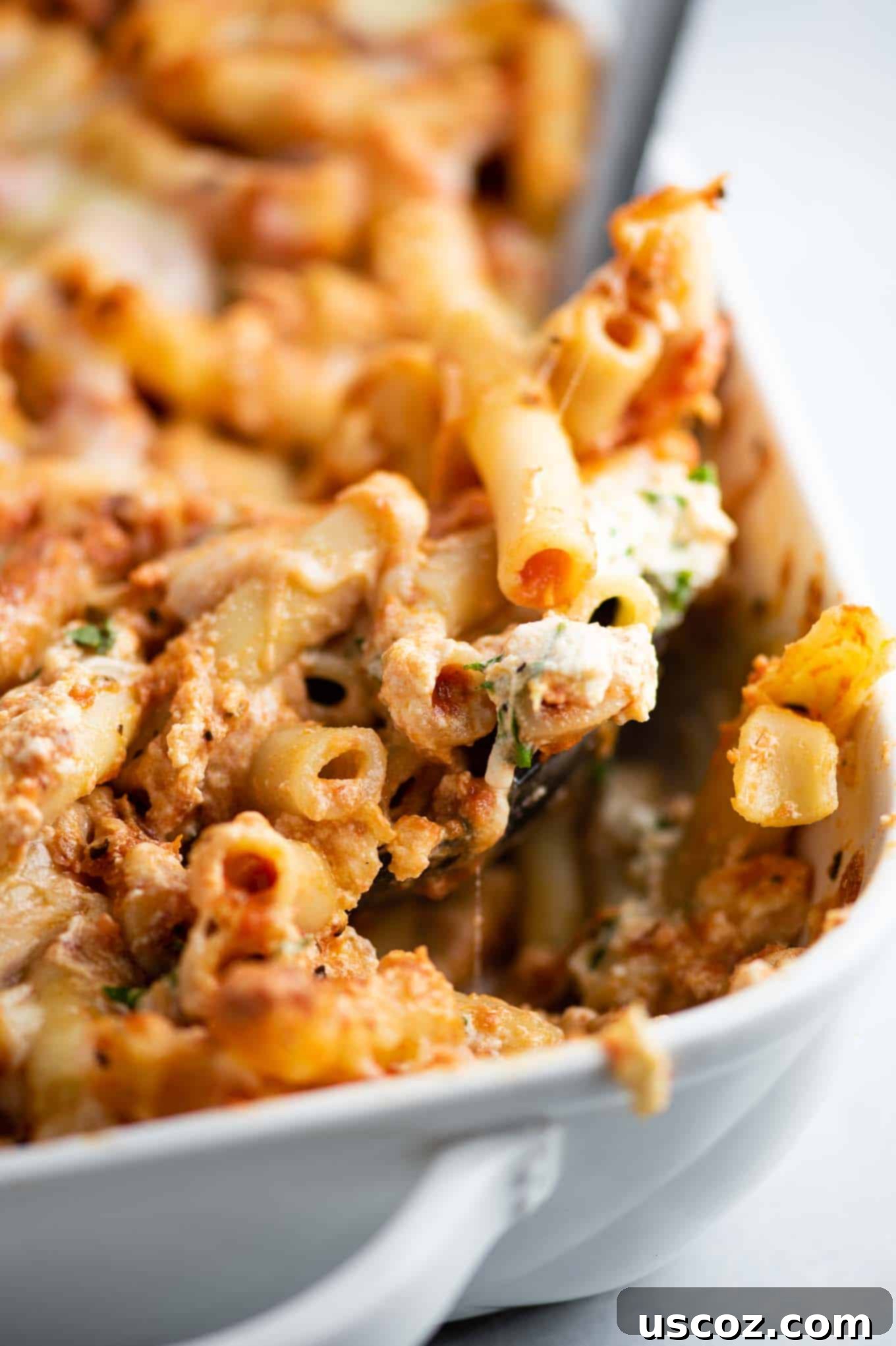 Ultimate Triple Cheese Baked Ziti 4 a spoon dishing out a scoop of ziti from the casserole pan, showing delicious layers of pasta and cheese