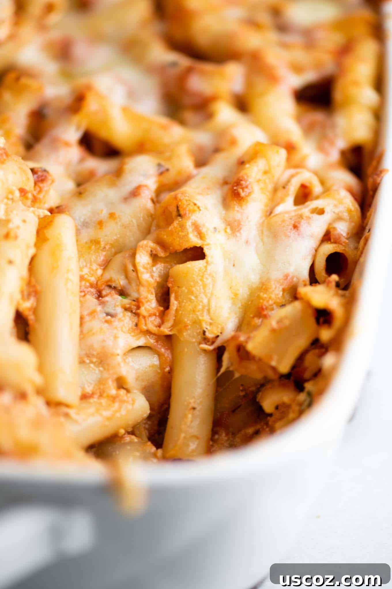 Ultimate Triple Cheese Baked Ziti 8 casserole dish with a spoon taken out, showcasing a generous serving of baked ziti ready to enjoy