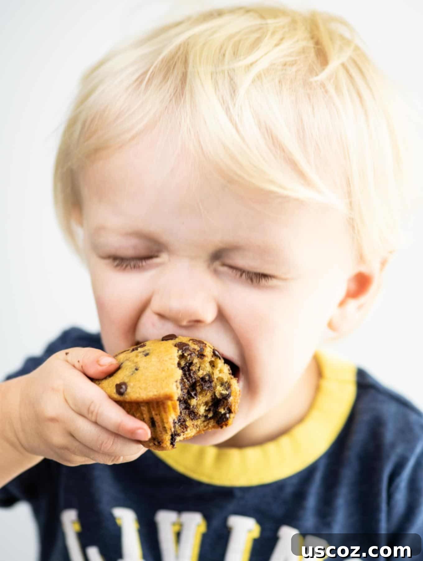 toddler taking a bite of a chocolate chip muffin