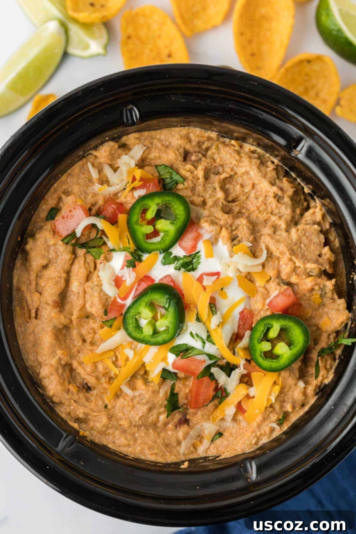 Slow Cooker Fiesta Bean Dip 2 bean dip in a crock pot topped with jalapenos, cheese, and tomatoes