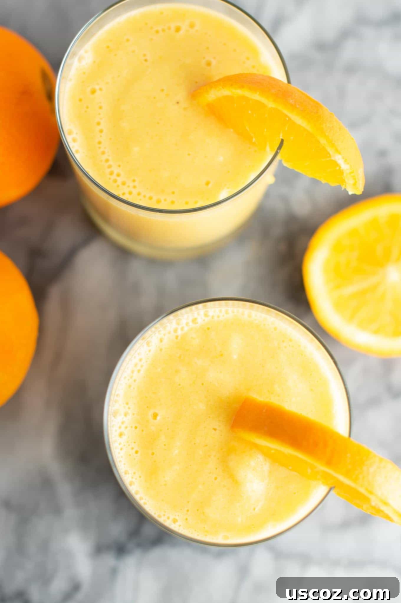 Sunshine Orange Smoothie 3 Overhead view of a single orange smoothie in a clear glass with an orange slice, surrounded by scattered fresh whole oranges.