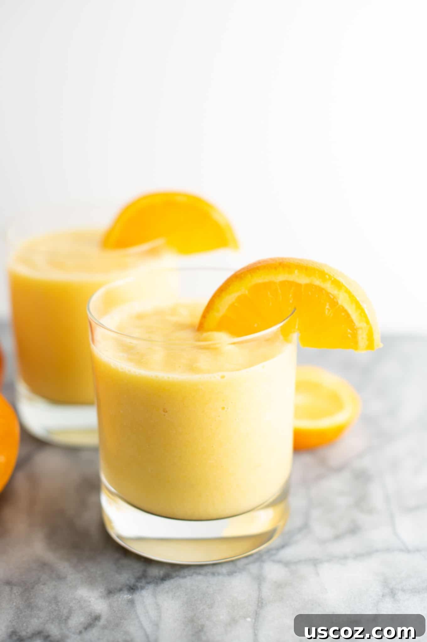 Sunshine Orange Smoothie 4 Two clear glasses showcasing refreshing orange smoothies, each beautifully garnished with a fresh orange slice on the rim.