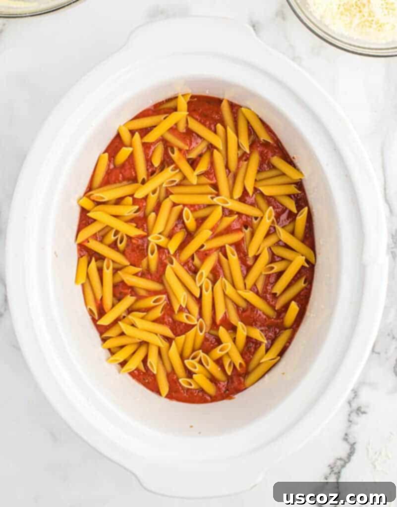 adding more penne pasta on top of the sauce