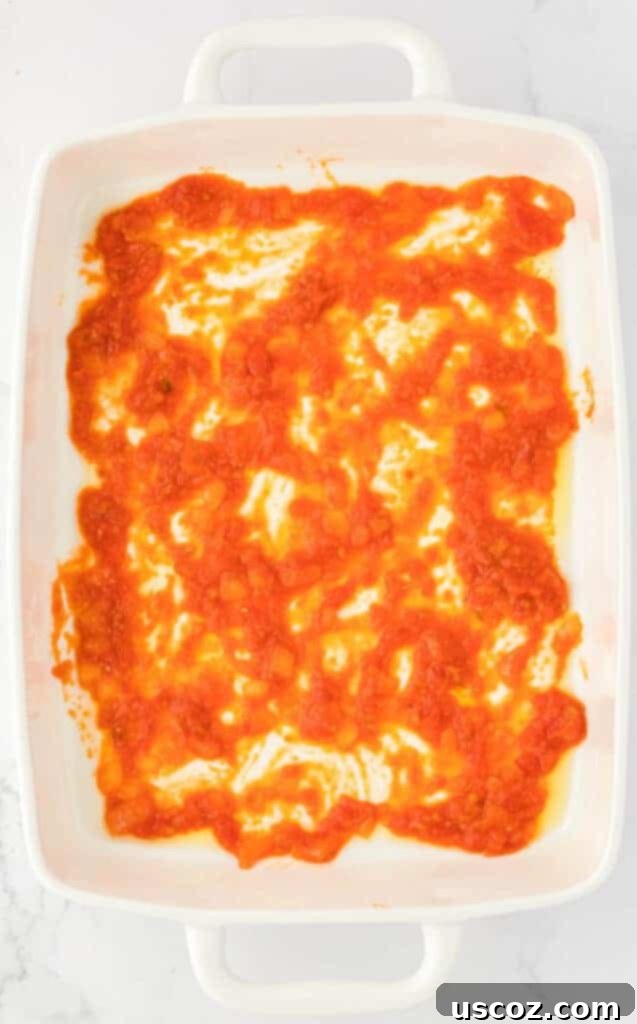 Classic Cheese Lasagna 10 A thin layer of vibrant red pasta sauce spread evenly at the bottom of a glass 9x13 baking dish, ready for the first layer of lasagna noodles.