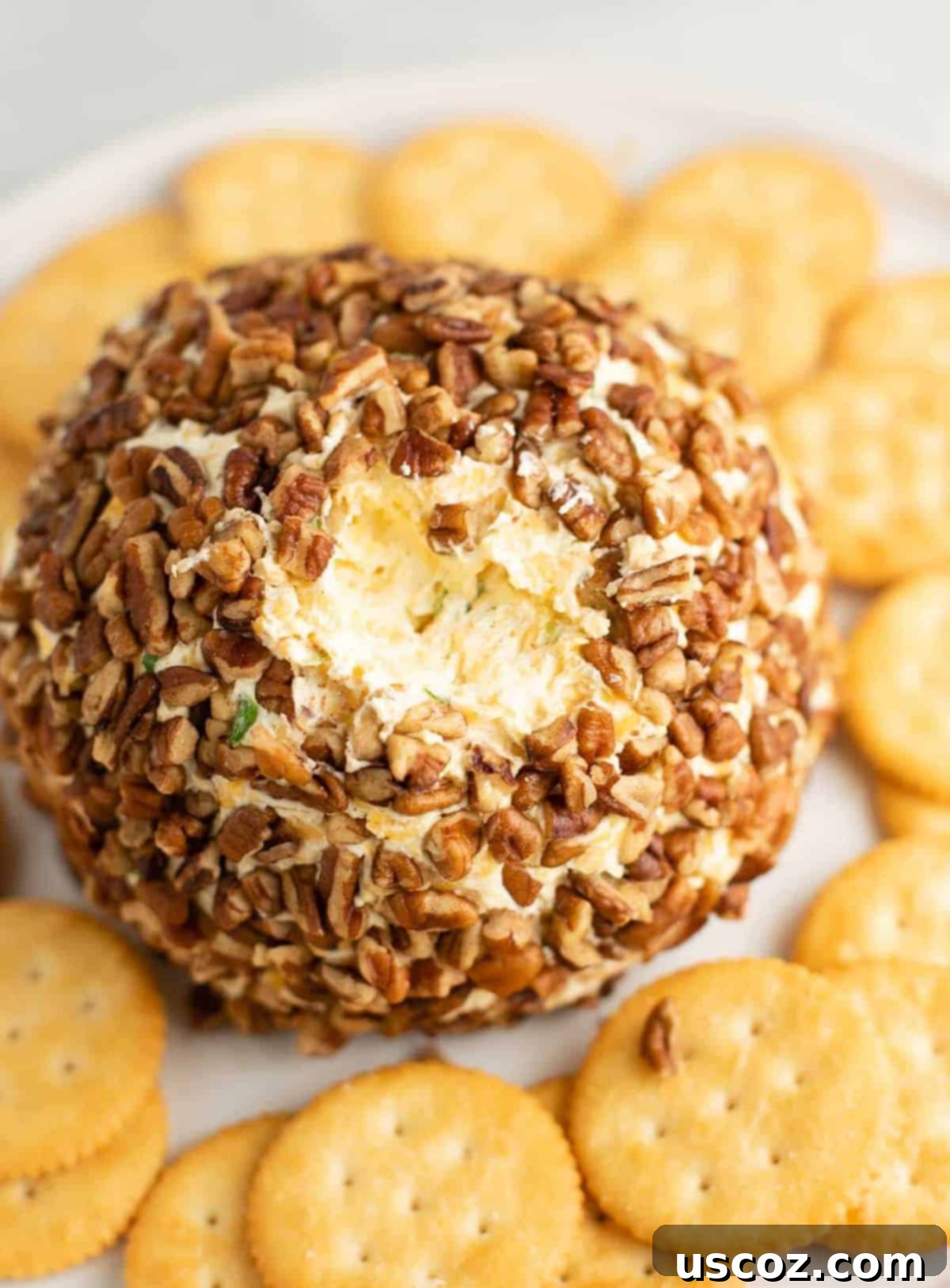 Party Perfect Cheese Ball 11 A close-up of a cheese ball with a small portion scooped out, revealing the creamy interior mixed with green onions and cheddar.