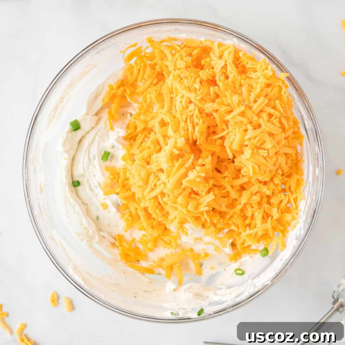 Party Perfect Cheese Ball 8 The cheese ball mixture in a bowl, with freshly shredded cheddar cheese already incorporated, chilling in the fridge.