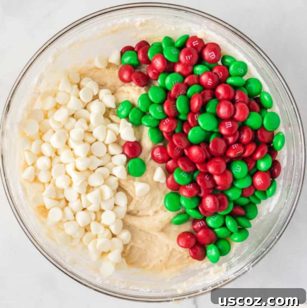 Merry Cookie Bar Magic 9 adding m&m's and white chocolate chips to the cookie bar batter in a mixing bowl