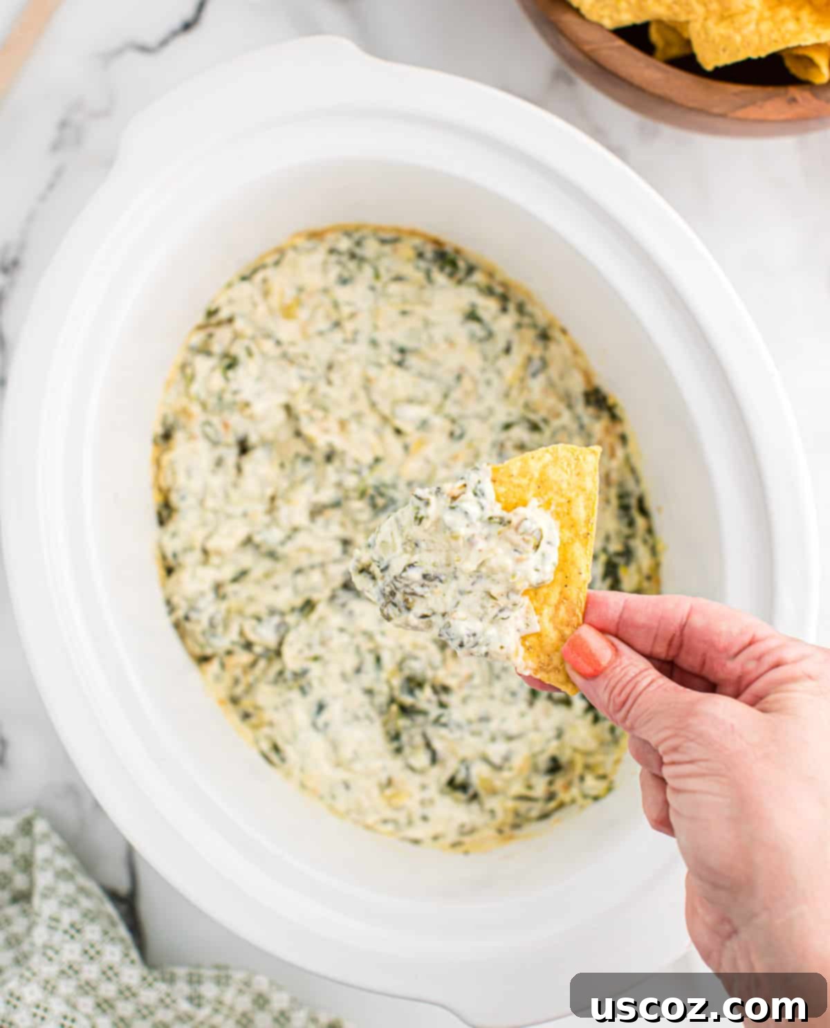 Creamy Slow Cooker Spinach Artichoke Dip 2 dipping a chip into a slow cooker full of spinach artichoke dip