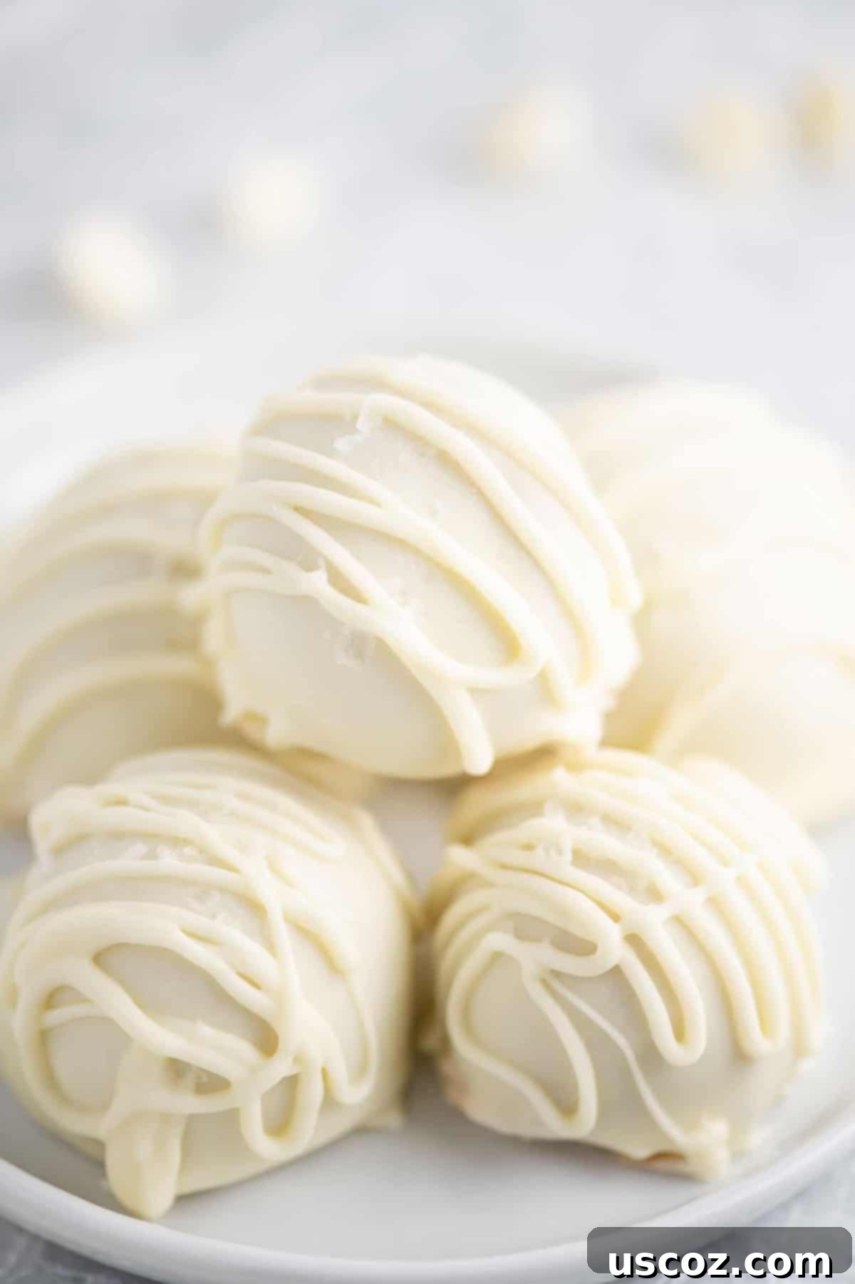 Decadent White Chocolate Peanut Butter Bliss Balls 2 white chocolate peanut butter balls with drizzle stacked on a white plate