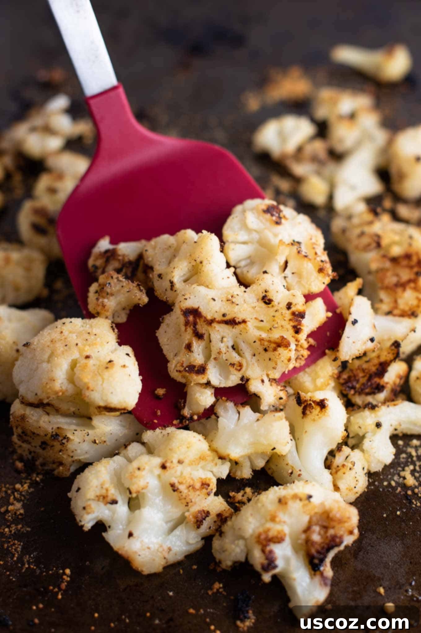 Crispy Roasted Frozen Cauliflower 7 A red spatula scooping up perfectly roasted, golden-brown cauliflower florets