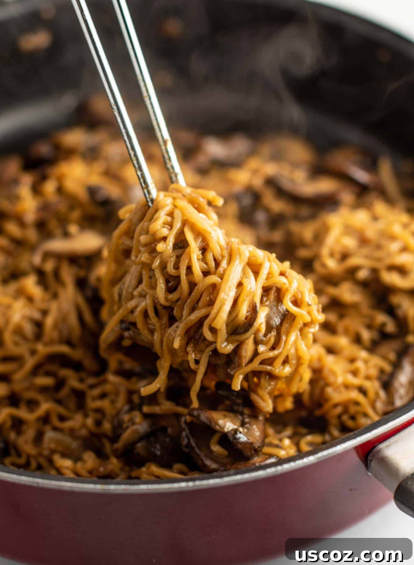 Umami Mushroom Ramen 2 Tongs pulling saucy mushroom ramen noodles from a large pan, showcasing perfectly coated strands.