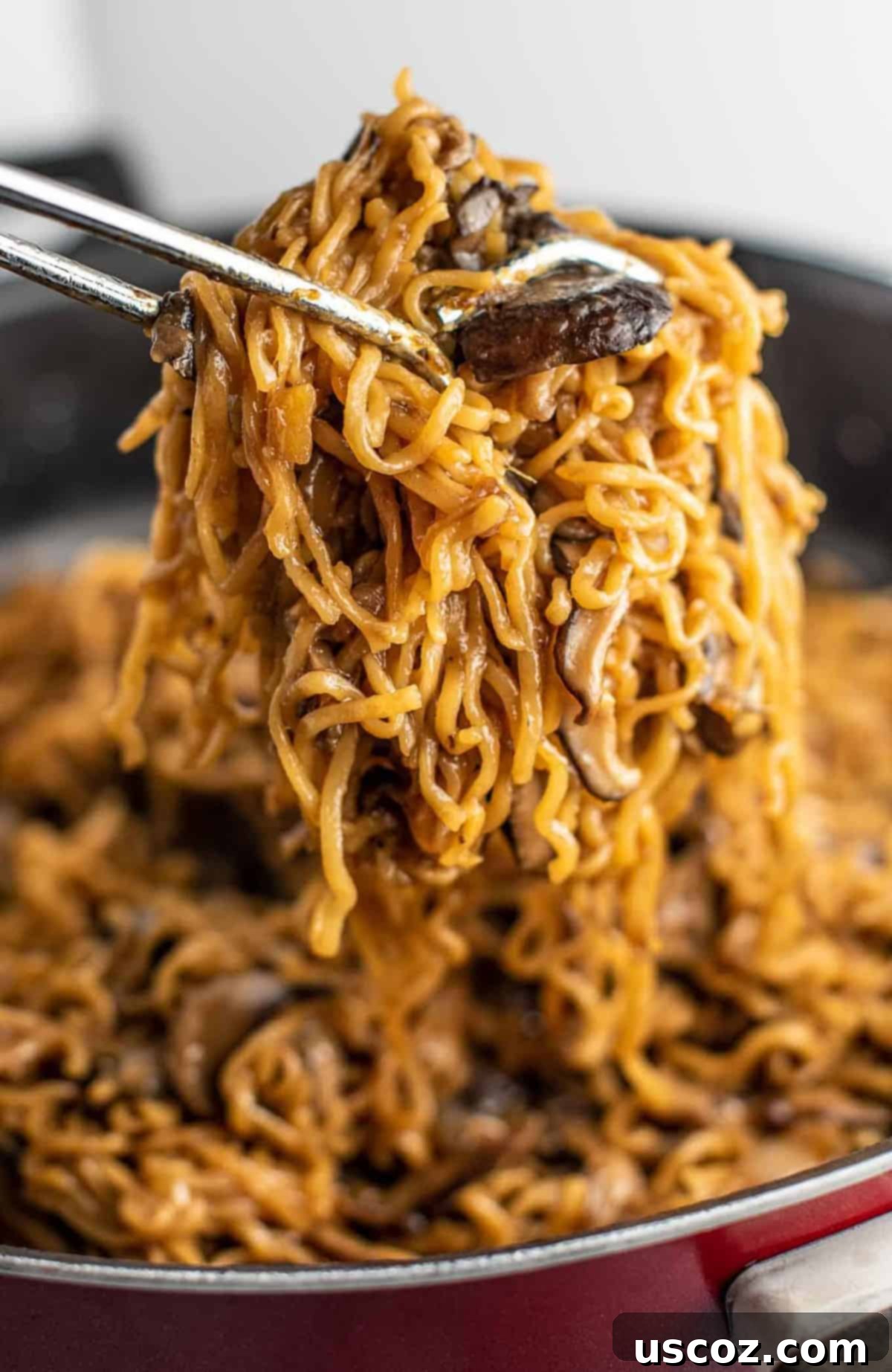 Umami Mushroom Ramen 9 Tongs mixing ramen noodles with cooked mushrooms and sauce in a pan, ensuring even coating.