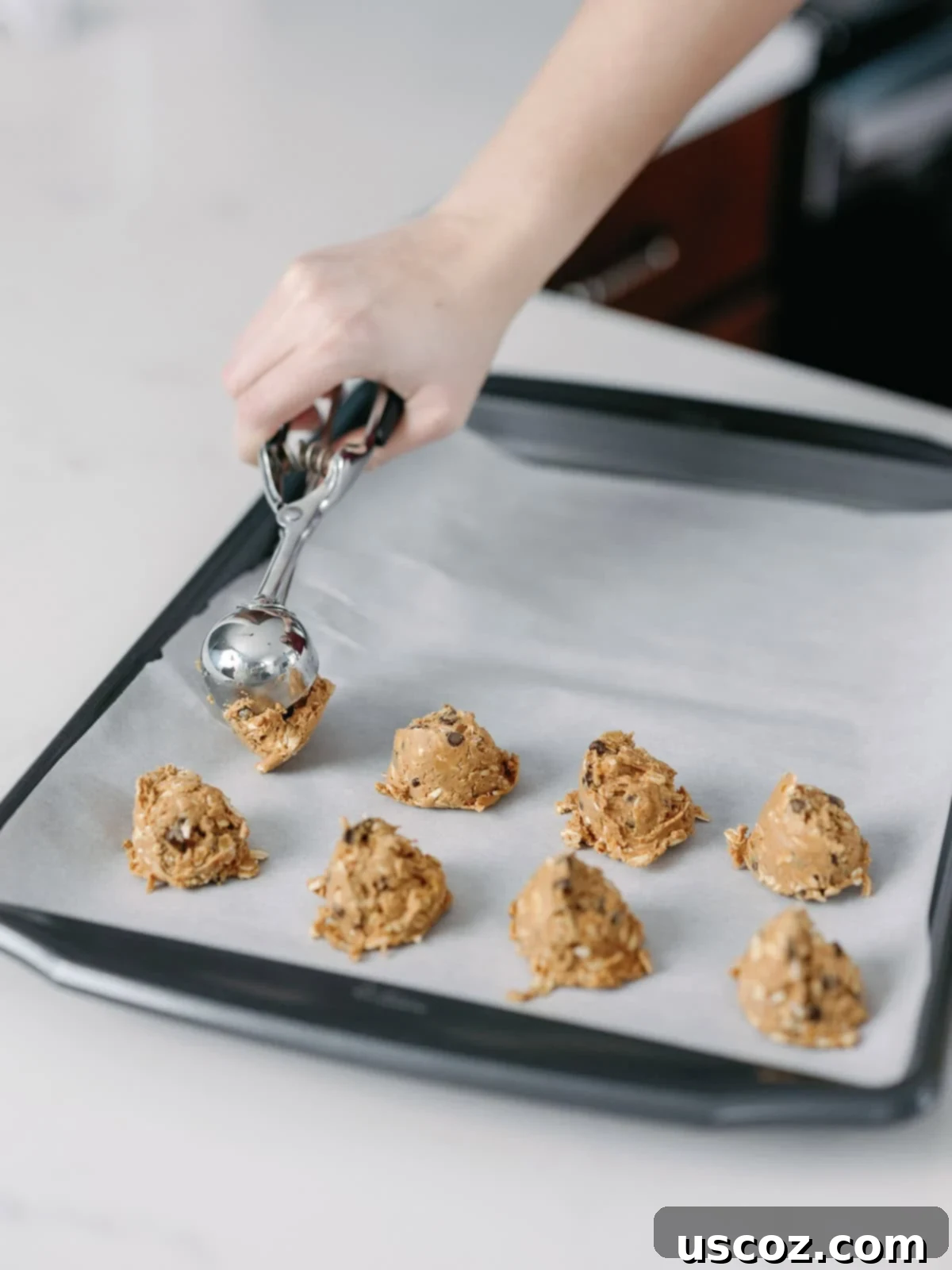 Wholesome Energy Bites 7 Someone using a mini cookie scoop to portion out energy ball batter onto a parchment-lined baking sheet