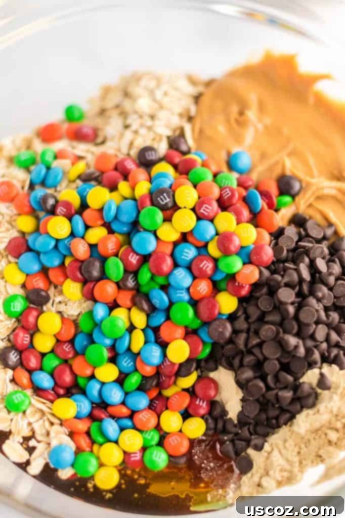 Monster Cookie Energy Bites 6 A close-up view of vibrant mini M&M's mixed into the energy ball batter in a clear mixing bowl, showcasing the colorful flecks.