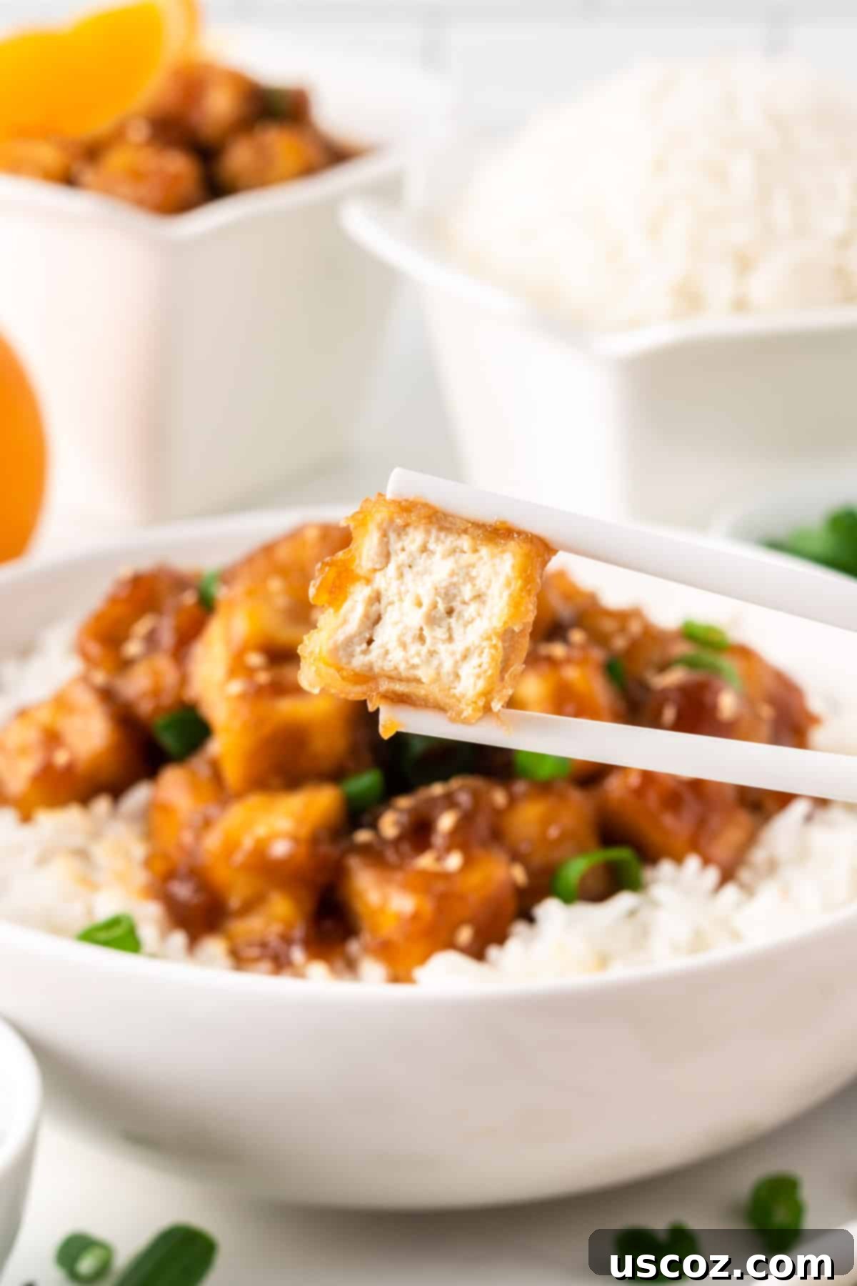 Zesty Orange Tofu 15 chopsticks holding a piece of orange tofu with a bite taken