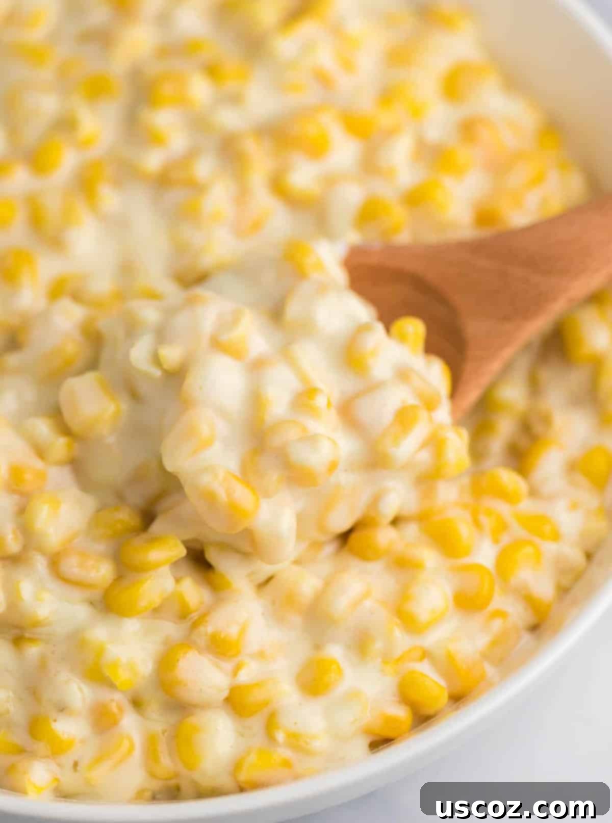 Dreamy Creamed Corn 2 A wooden spoon taking a scoop of creamy, golden creamed corn from a serving dish, highlighting its rich texture and appealing presentation.