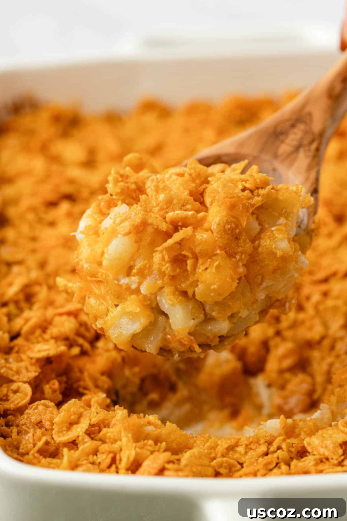 Crispy Cheesy Potato Casserole 2 A scoop of golden-brown funeral potatoes with a crispy corn flake topping being lifted from a baking dish, ready to be served.
