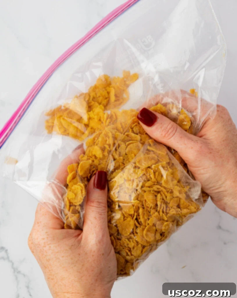 Crispy Cheesy Potato Casserole 12 Hands crushing corn flakes inside a ziploc bag to create a coarse topping texture for the casserole.