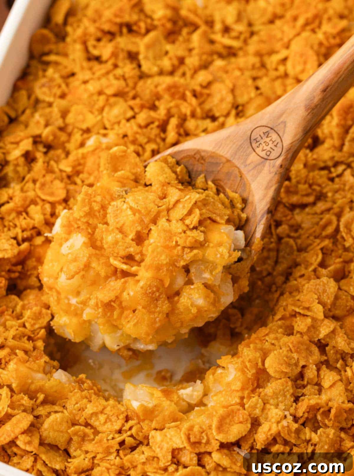 Crispy Cheesy Potato Casserole 16 A serving spoon lifting a portion of hot, gooey funeral potatoes from the baking dish, revealing the creamy interior and melted cheese.