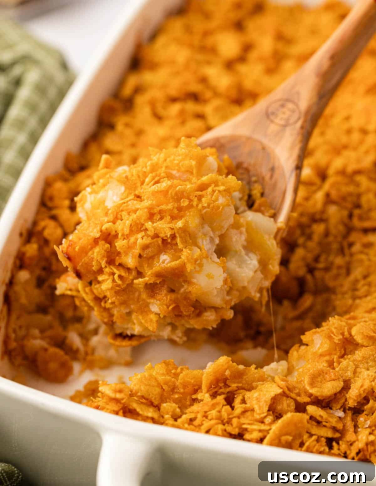Crispy Cheesy Potato Casserole 18 A serving spoon digging into a freshly baked dish of funeral potatoes, showing the warm, creamy texture and golden topping, ready to be enjoyed.
