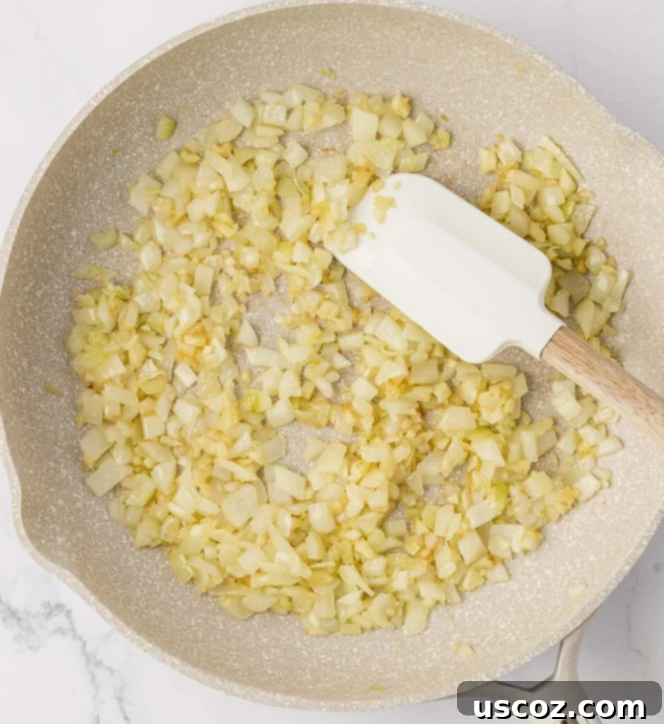 Crispy Cheesy Potato Casserole 6 Close-up of diced garlic and onion cooking until softened in a buttered skillet, showing their translucent texture.
