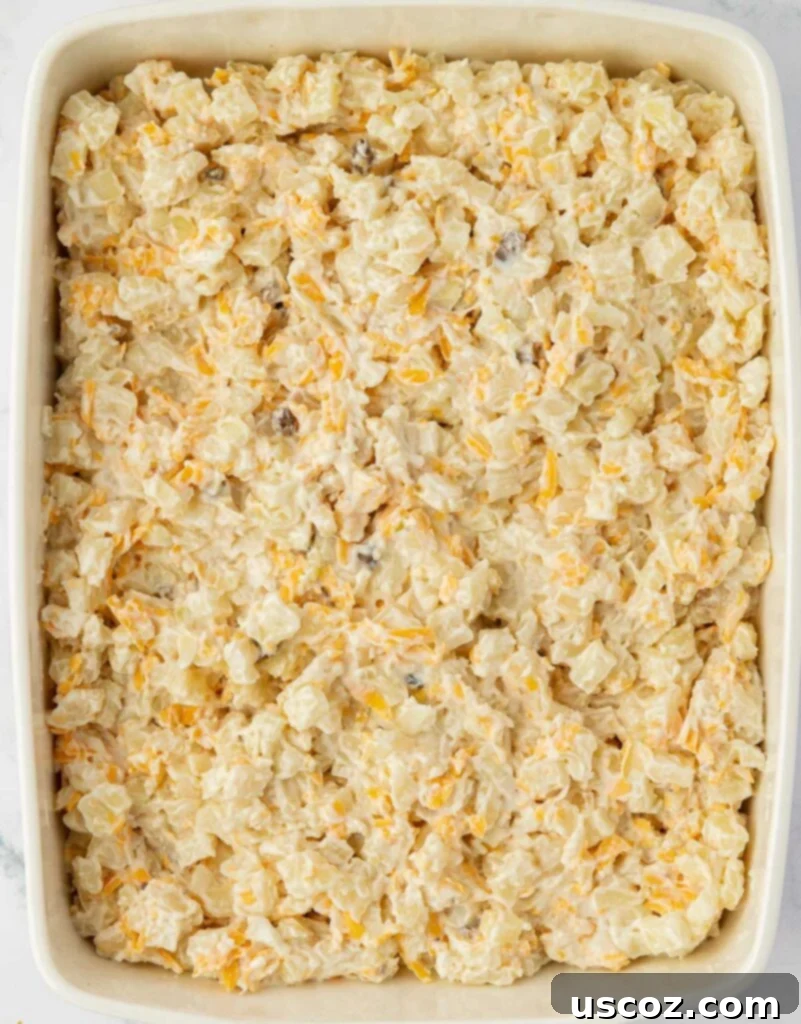 Crispy Cheesy Potato Casserole 9 Creamy hash brown potato mixture spread evenly into a 9x13 inch glass baking dish, ready for topping.