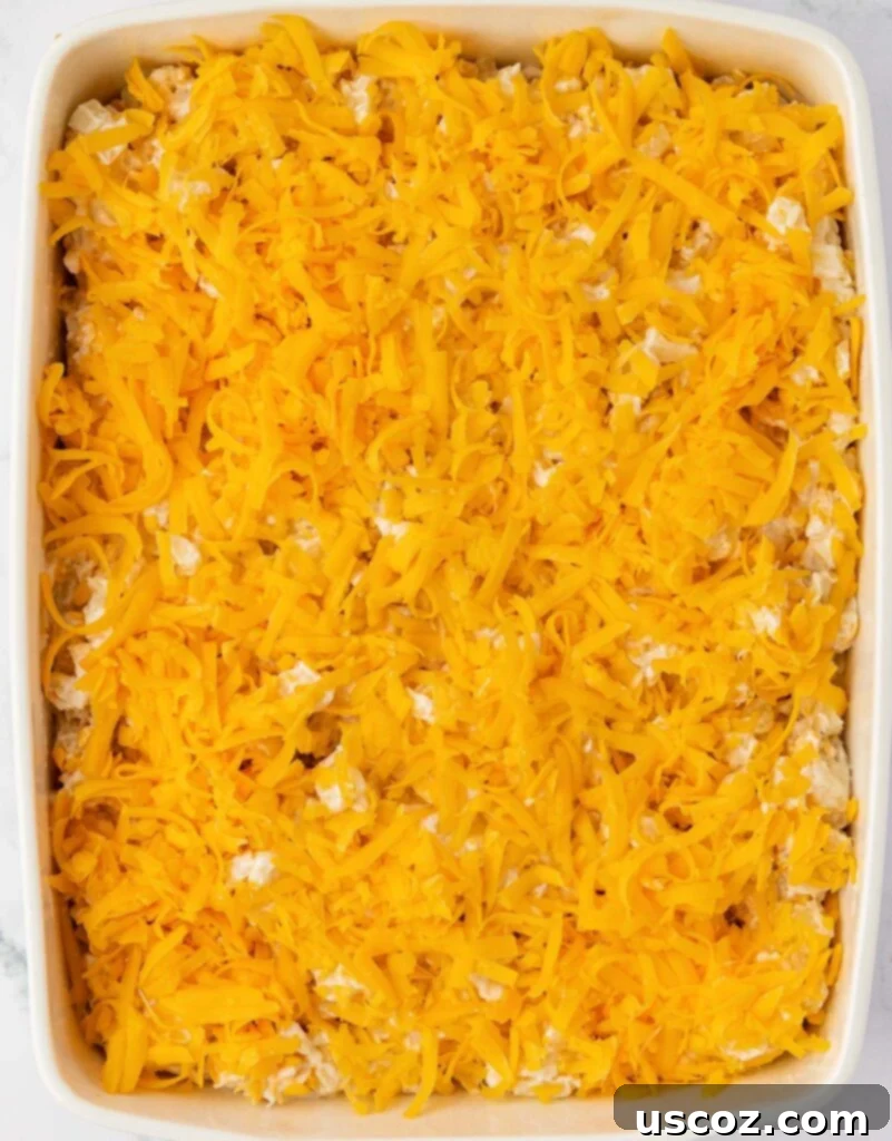 Crispy Cheesy Potato Casserole 10 The hash brown potato mixture in the baking dish, generously topped with a layer of shredded cheddar cheese, ready for the corn flake crust.