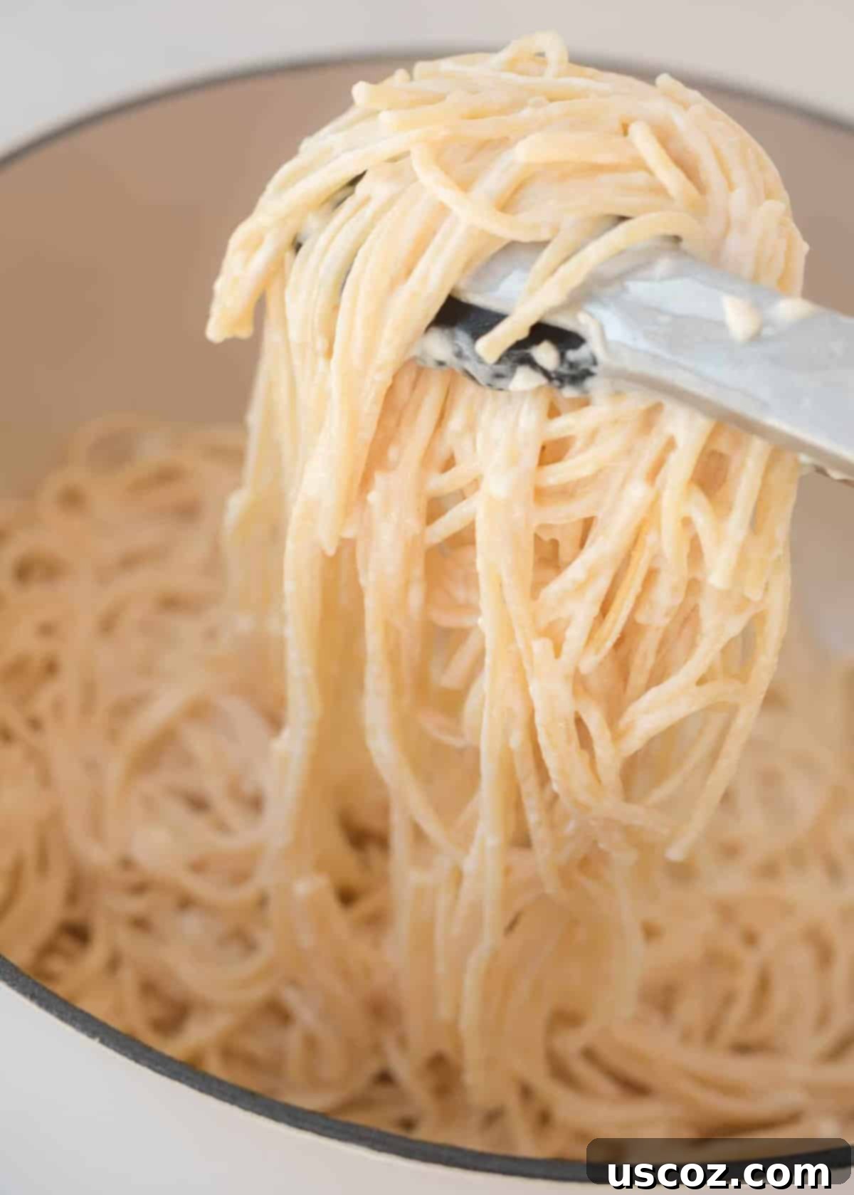 Velvety Cream Cheese Pasta 2 Tongs grabbing cream cheese spaghetti noodles from a pan, highlighting the creamy texture.