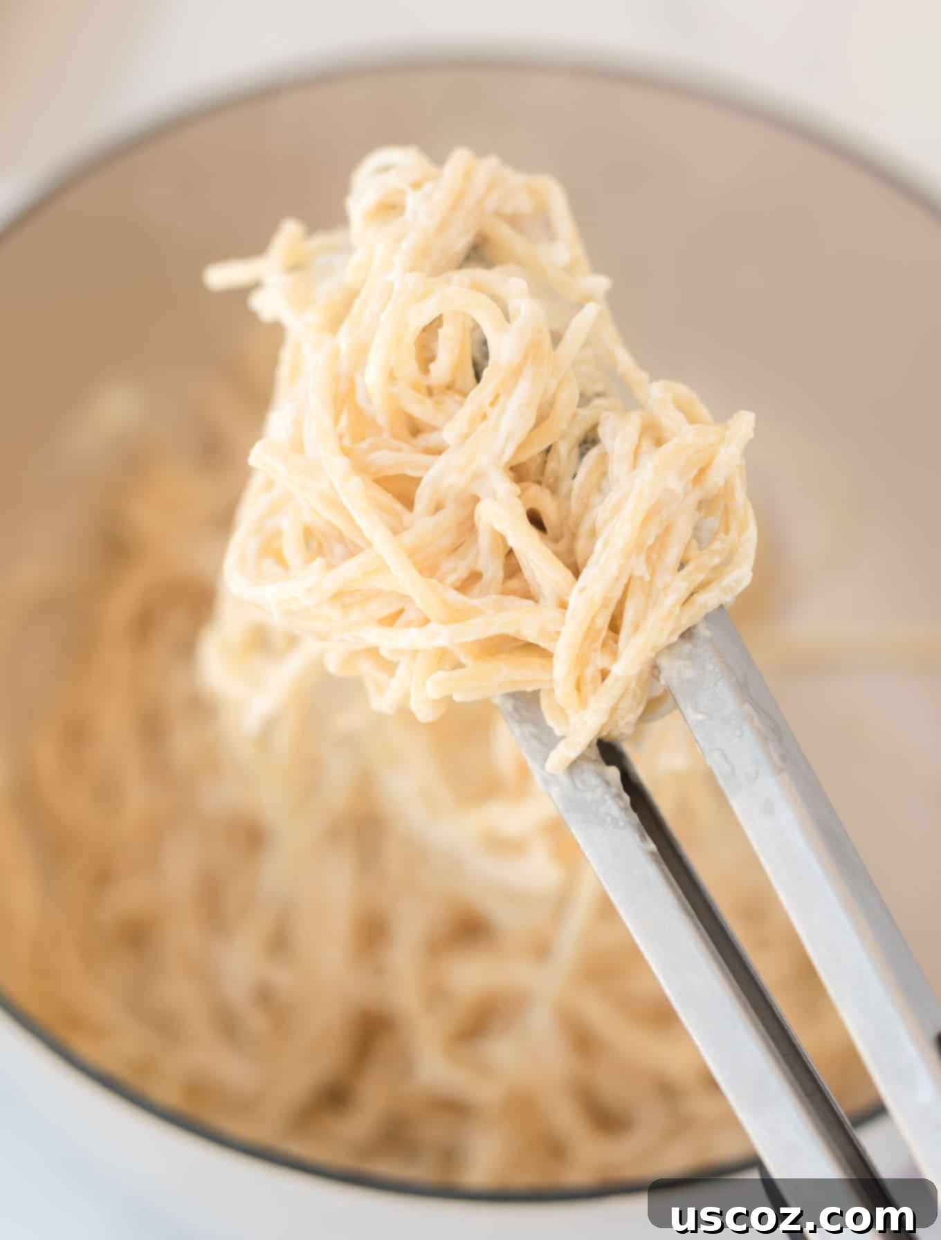 Velvety Cream Cheese Pasta 3 A close-up of cream cheese spaghetti noodles being served from a pan with tongs, showing the glossy sauce.