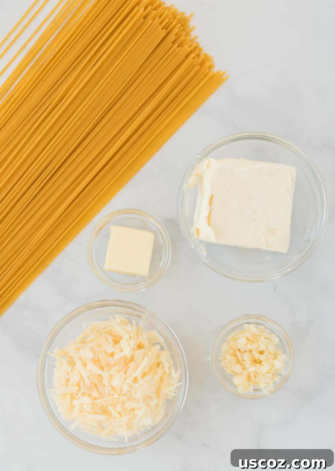 Velvety Cream Cheese Pasta 4 Ingredients laid out on a counter: spaghetti noodles, a stick of butter, garlic cloves, cream cheese block, and a wedge of Parmesan cheese.