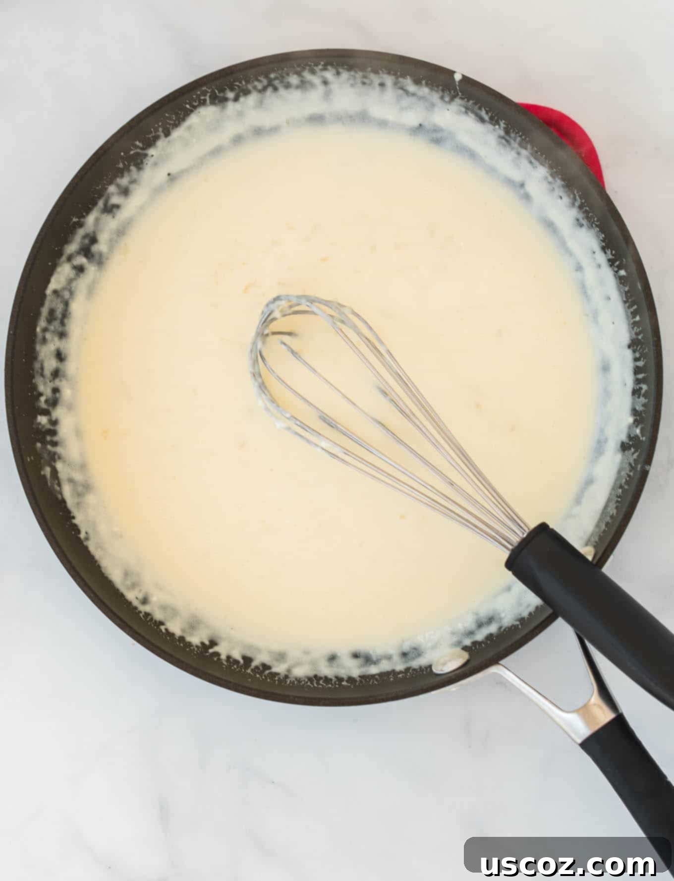 Velvety Cream Cheese Pasta 5 Cream cheese pasta sauce being whisked in a stainless steel skillet, showing its smooth, creamy texture.