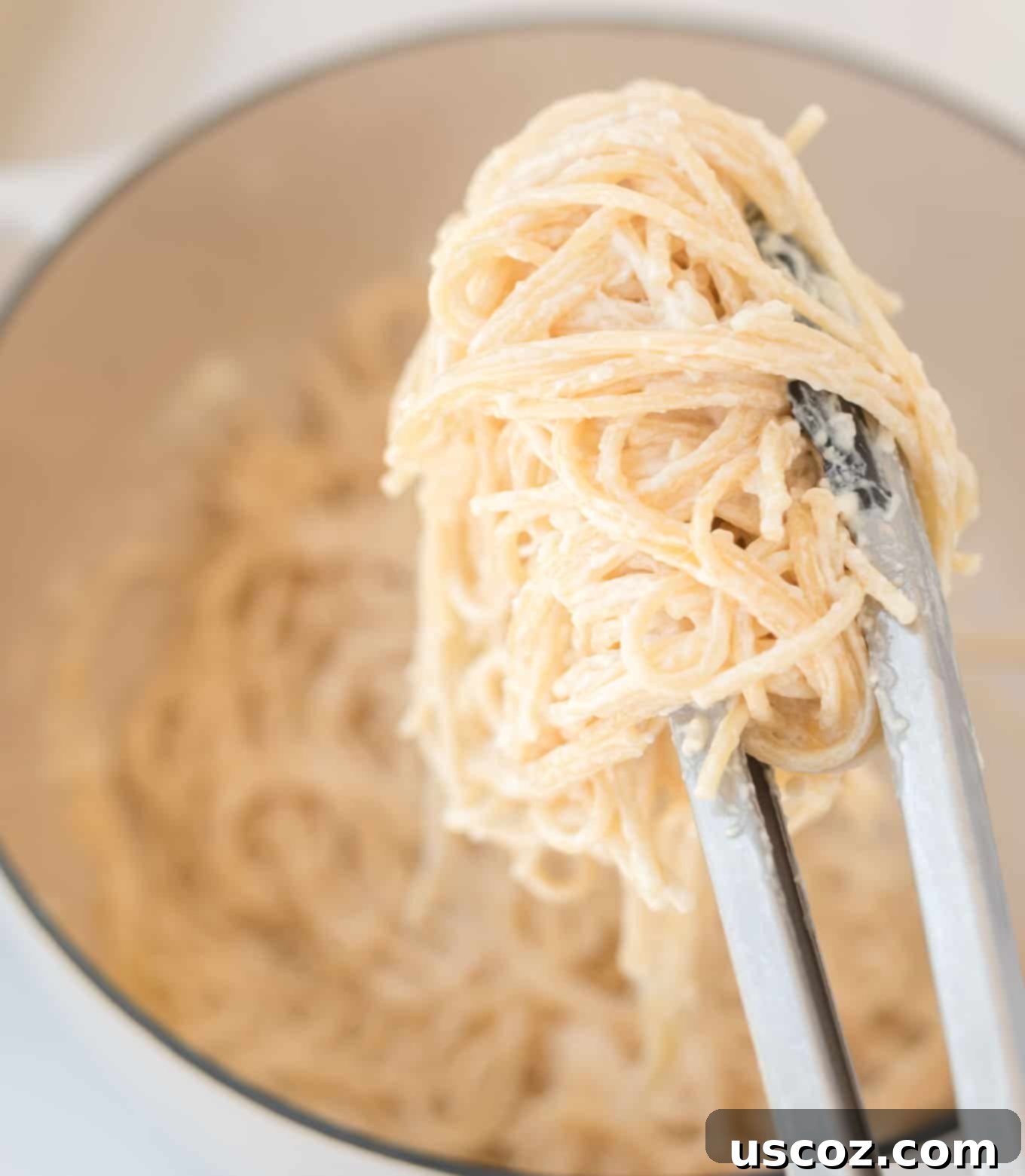 Velvety Cream Cheese Pasta 8 Creamy cream cheese pasta in a pan, with a hand holding tongs to serve.