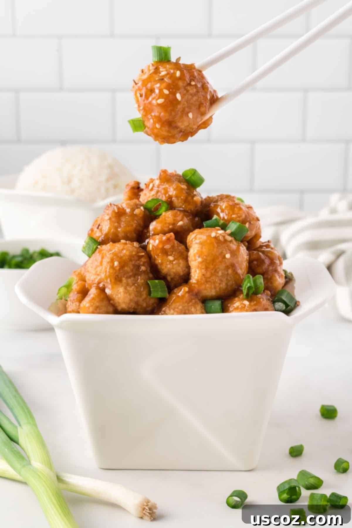 Sticky Teriyaki Cauliflower Bites 2 Chopsticks taking a bite of crispy teriyaki cauliflower from a serving container, showcasing its rich glaze and appealing texture.
