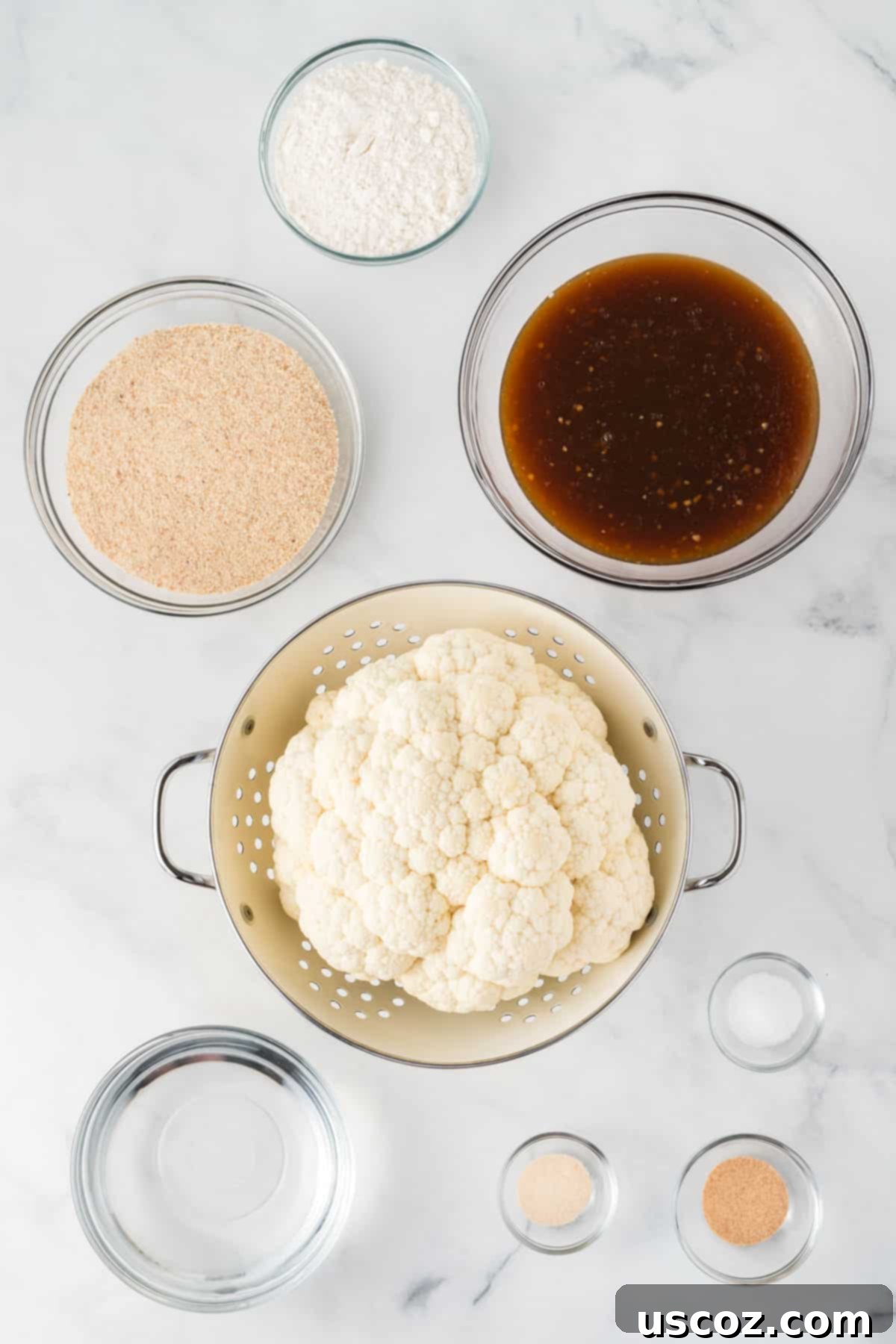 Sticky Teriyaki Cauliflower Bites 4 A selection of fresh ingredients laid out, including a head of cauliflower, flour, panko bread crumbs, garlic powder, onion powder, salt, and ingredients for homemade teriyaki sauce, illustrating everything needed to make the dish.