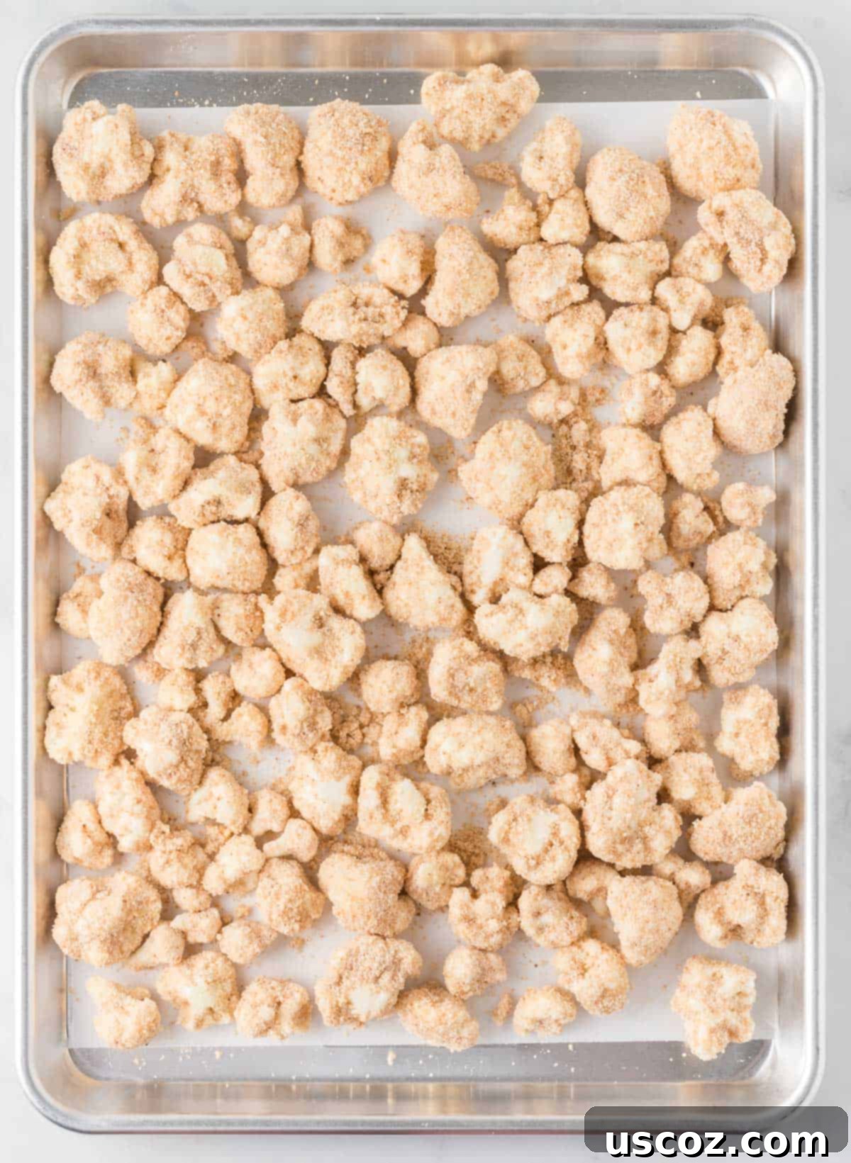 Sticky Teriyaki Cauliflower Bites 8 Battered and breaded cauliflower florets arranged on a parchment-lined baking sheet, ready for the oven.