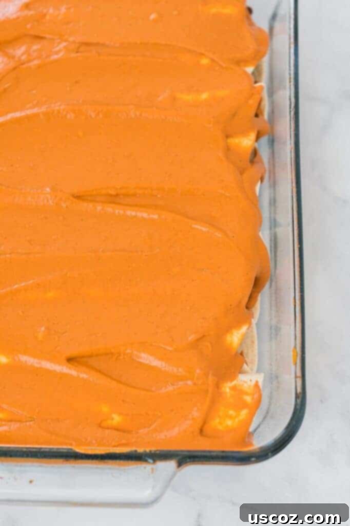 Ultimate Plant-Based Enchiladas 7 enchiladas rolled up in a casserole dish and topped with cashew queso